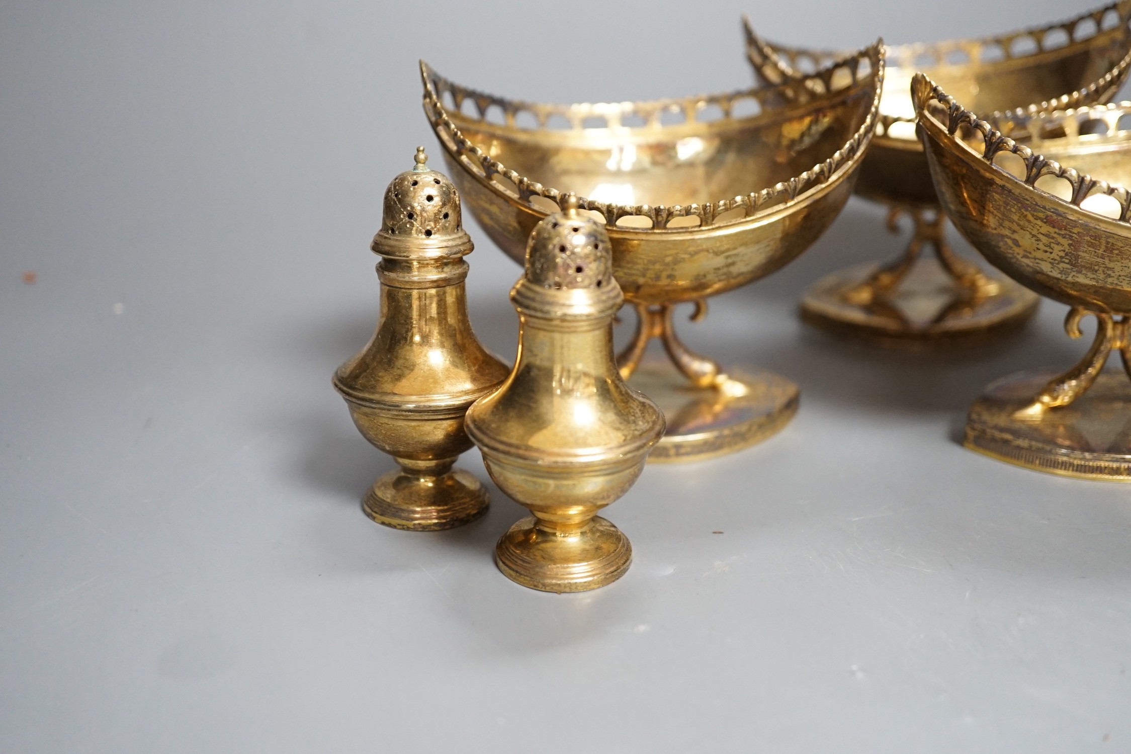 A set of four 20th century Spanish gilt white metal boat shaped pedestal bowls, with pierced borders, on twin dolphin supports 10.3cm and a set of four similar pepperettes, 18oz.